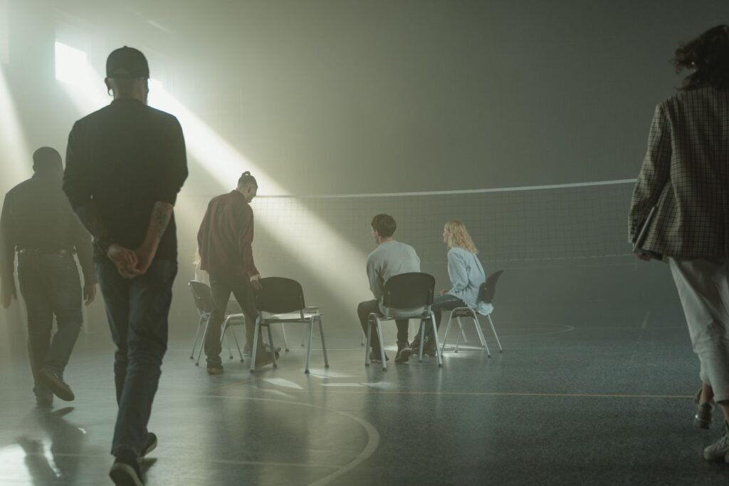 A group therapy session with diverse adults in a dimly lit gymnasium, highlighting mental health support.